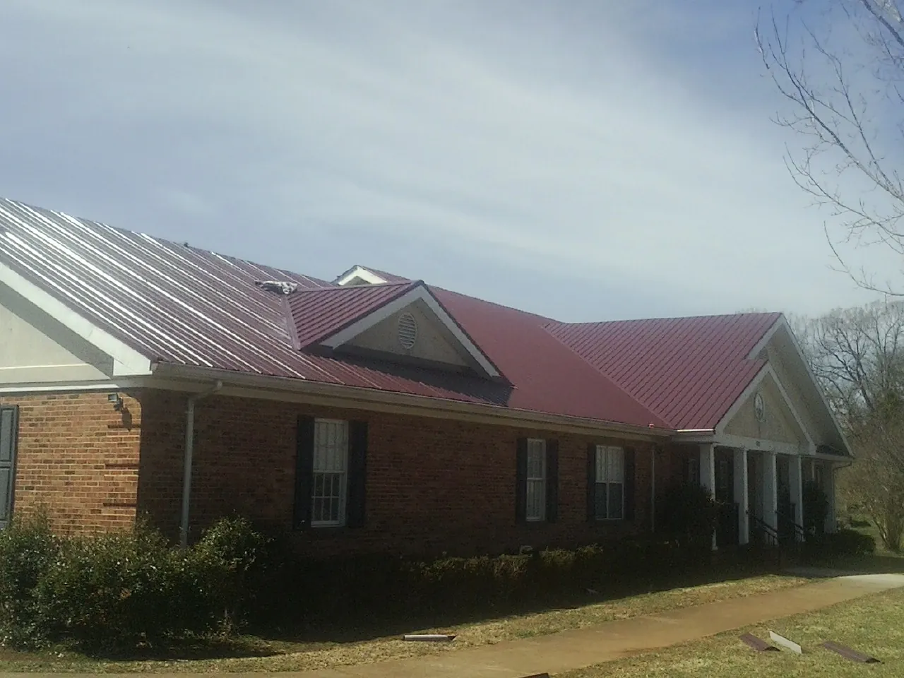 Red metal roof with gabled entries on a long brick building, from a Hail Damage Roof Repair job in Rocky Mount