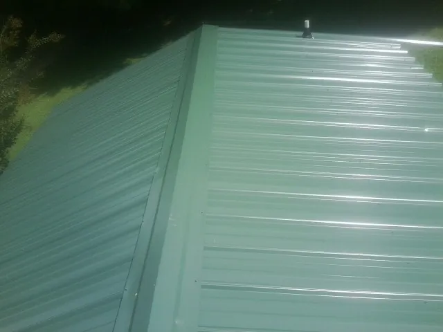 New green metal panels meeting at the ridge of a roof — Flat Roof Repair work by our crew in Rocky Mount