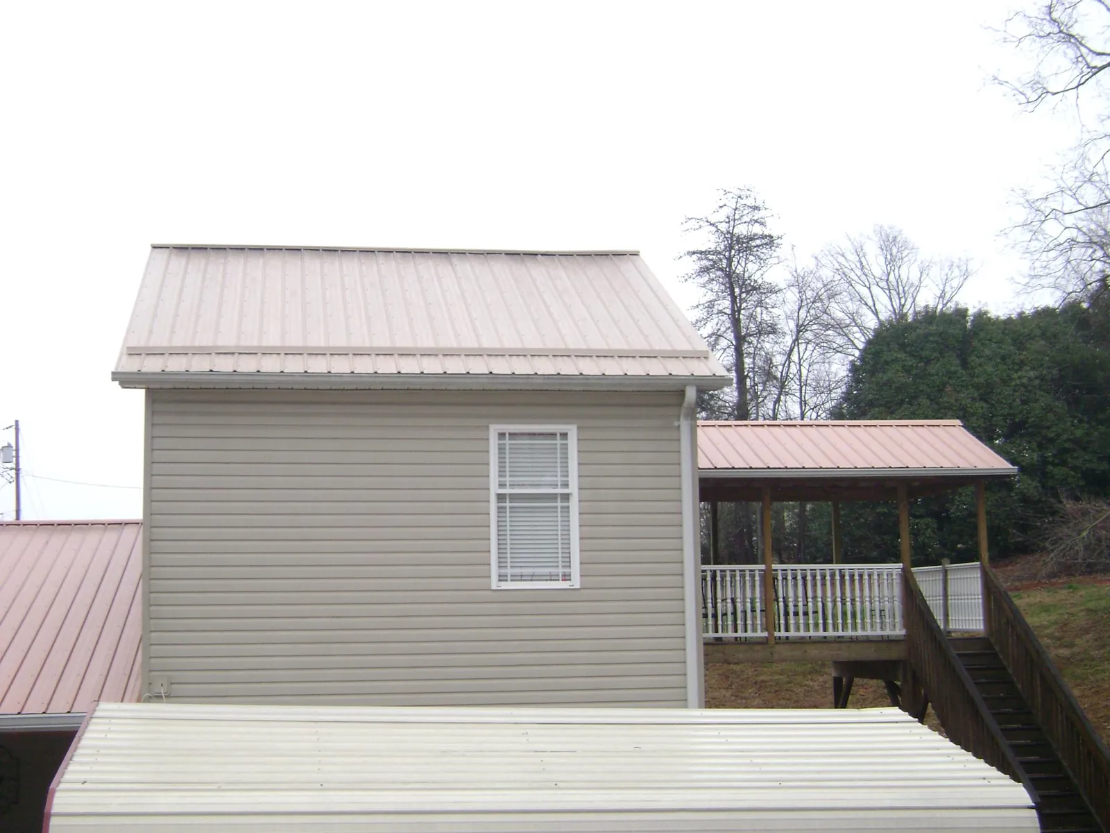 Tan metal roofs on a two story addition and attached porch, from a Roof Replacement job in Rocky Mount